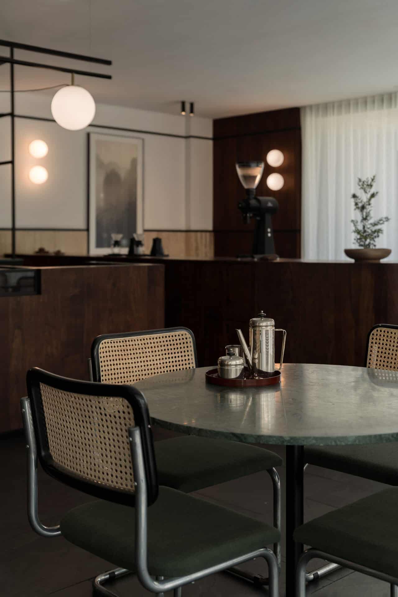 Green marble table and cane chairs beneath globe lights at Rosetta Roastery