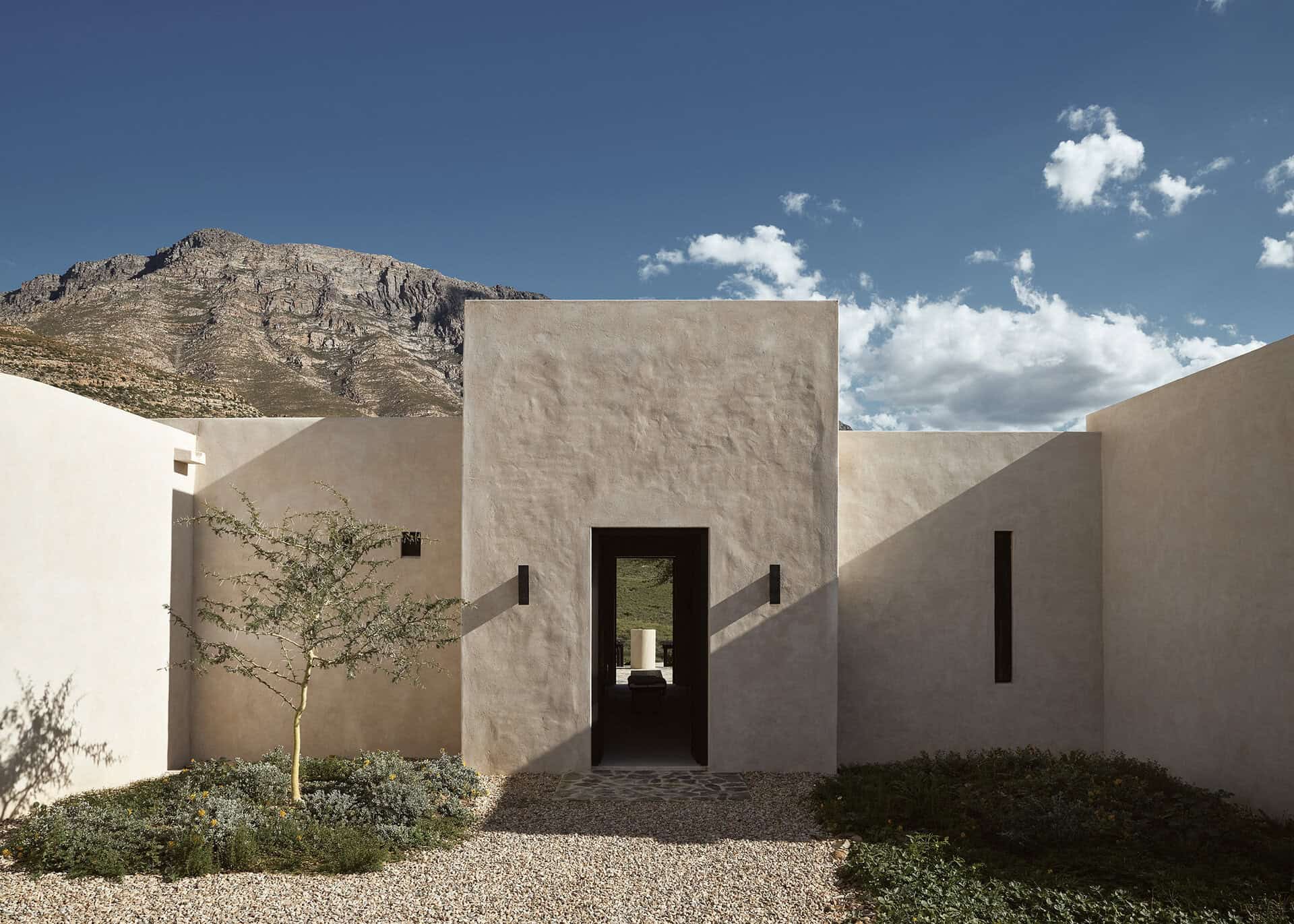 Entrance to Mura, rendered walls framing a recessed doorway with the mountains behind