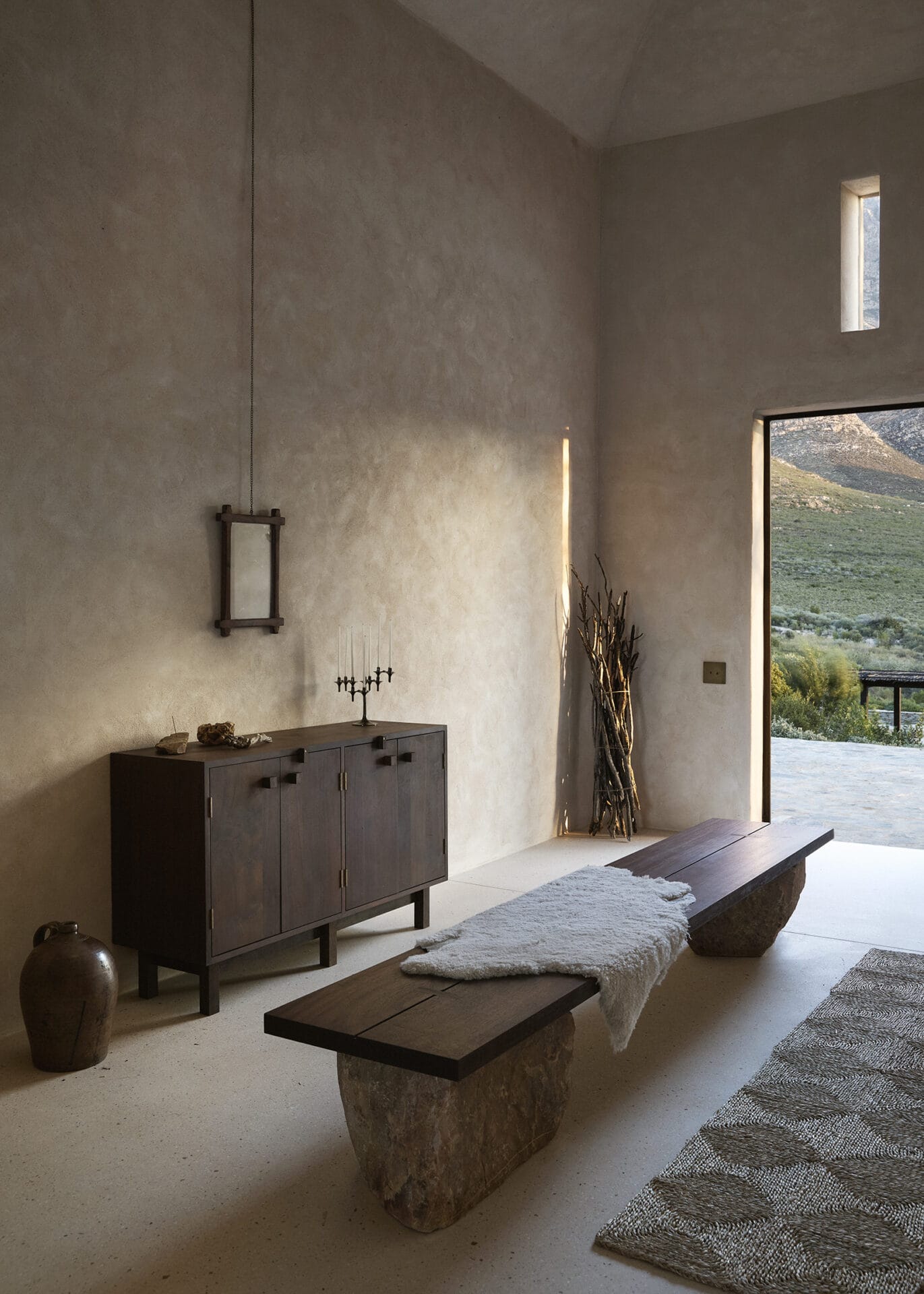 Entrance hall at Mura with a dark timber sideboard, stone bench and view to the veld
