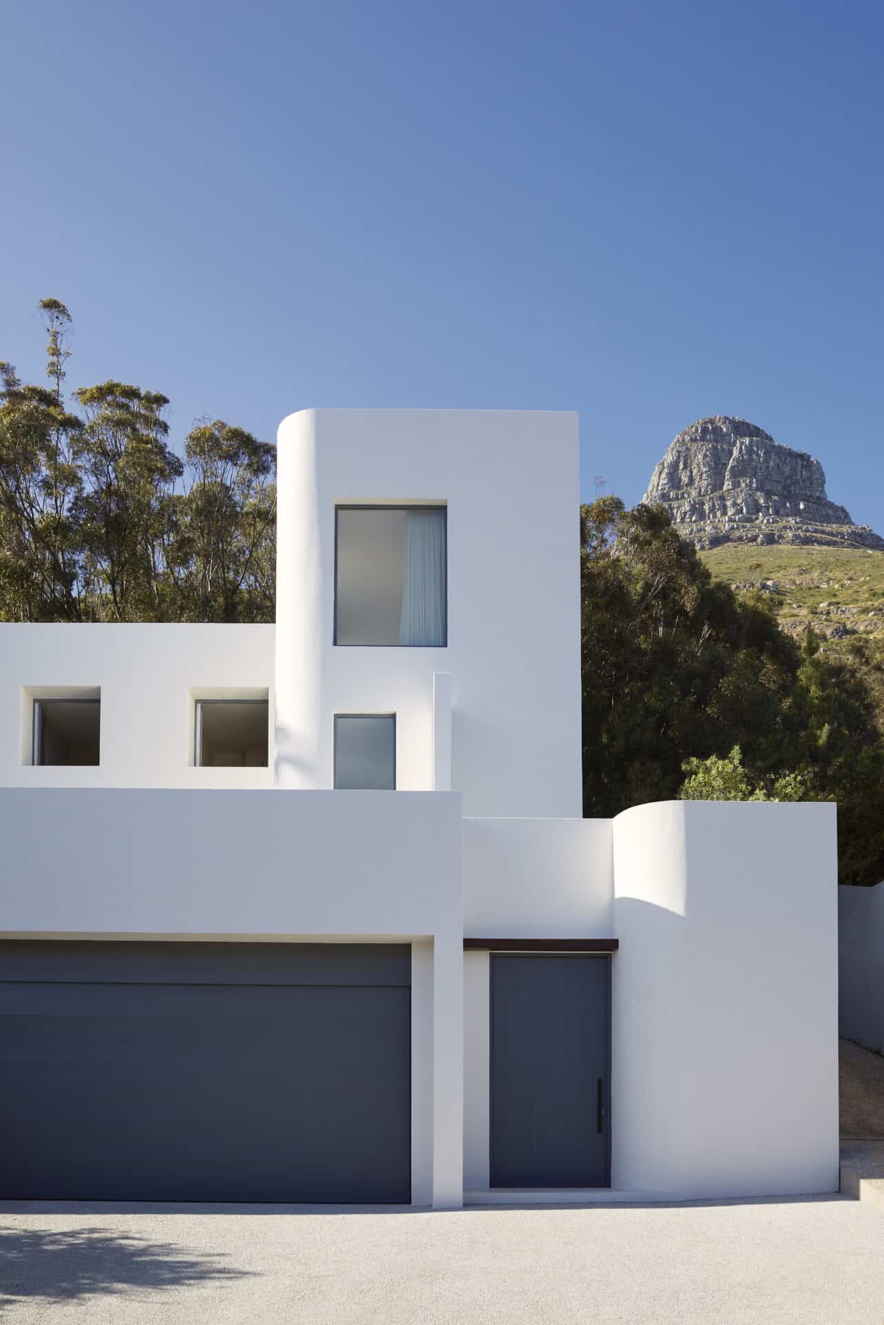 White rendered street facade of House T in Fresnaye, with the mountain rising behind