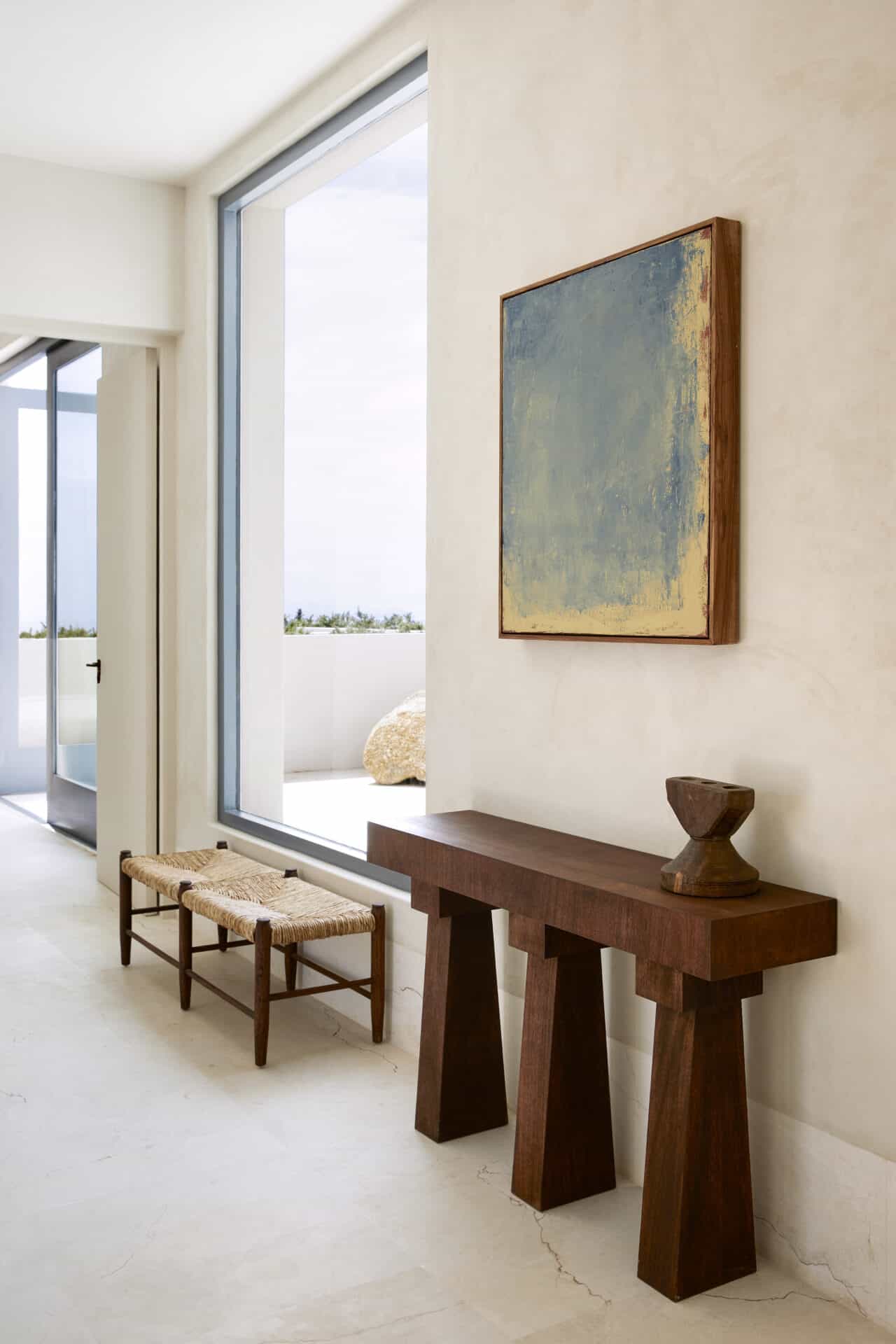 Timber console and painting in the hall at House T beside a full-height window