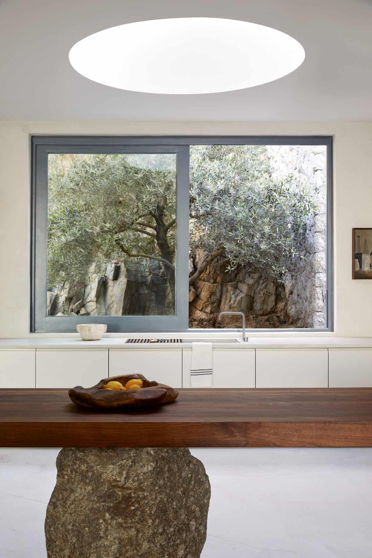 Window seat at House T framing an olive tree, lit by a circular rooflight