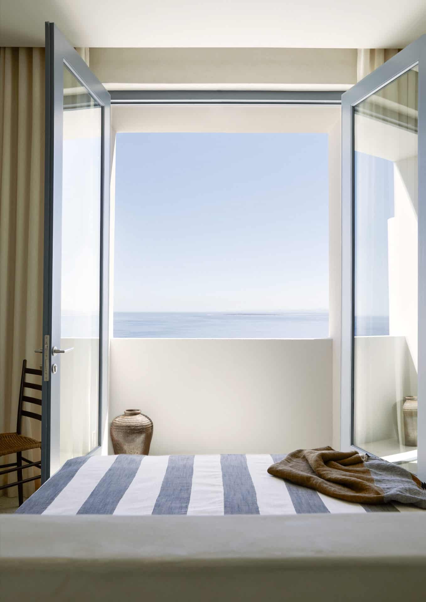 Bedroom at House T with striped linen and doors opening to the sea